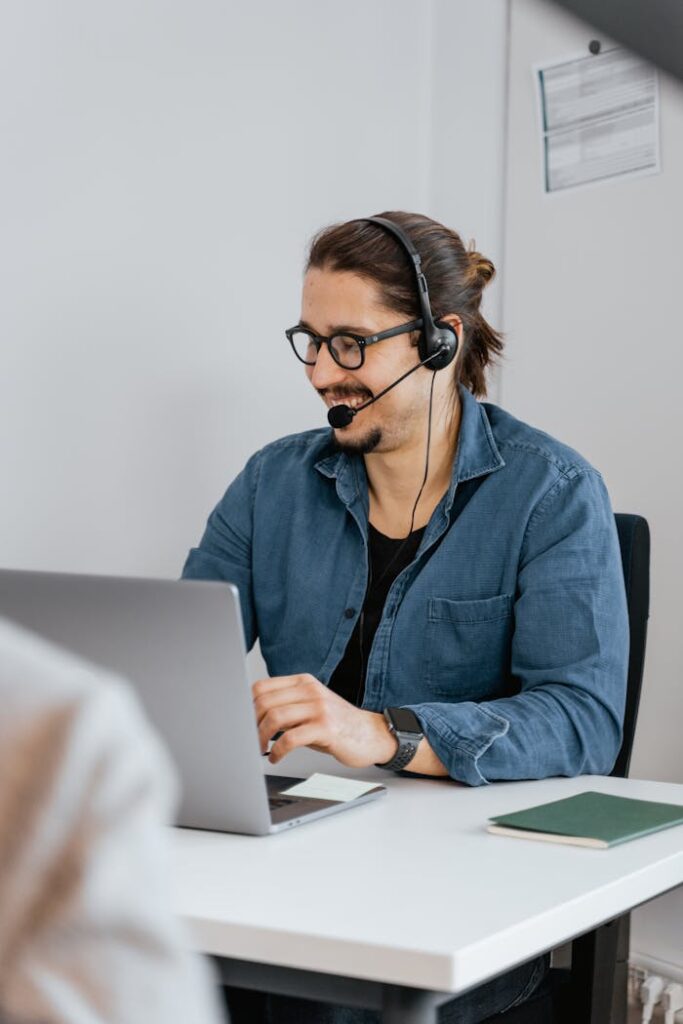 Business professional wearing glasses and headset working at laptop in office setting.